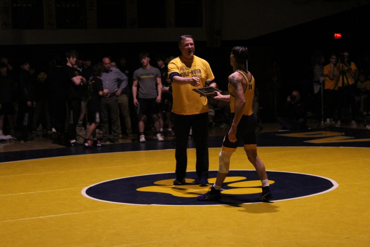 Senior Del Val wrestler Jaden Perez receives the 100 win plaque after he pinned his opponent.