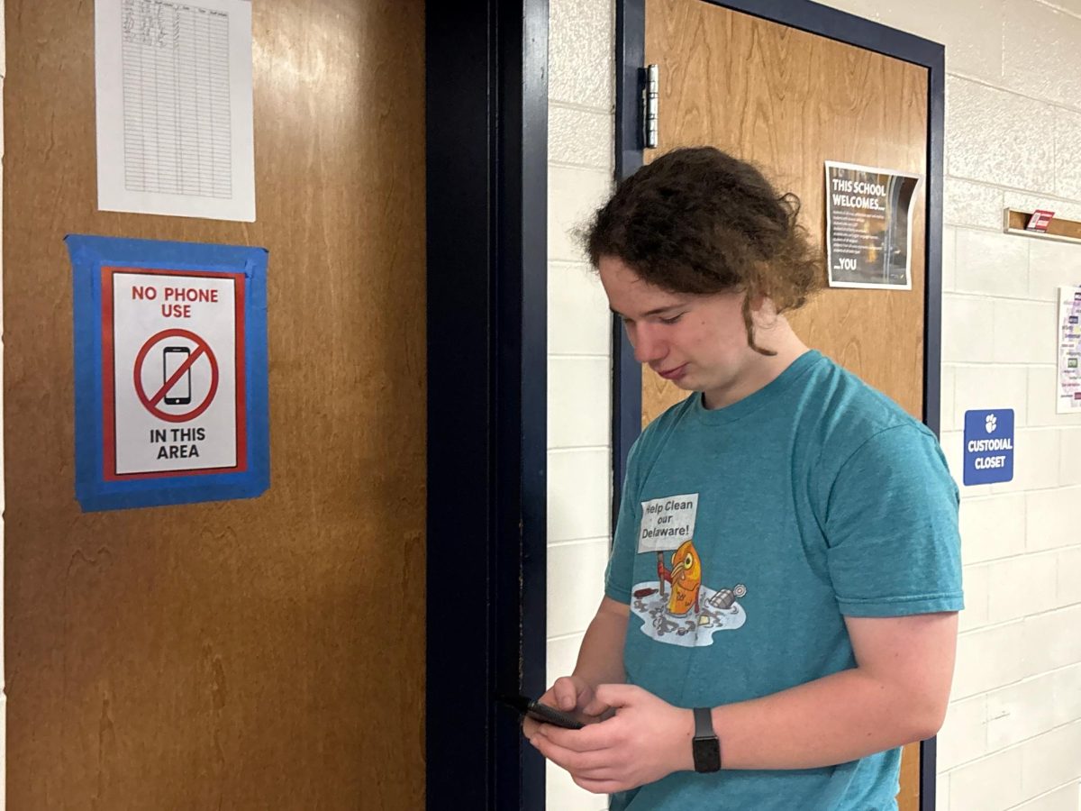 Del Val Freshman Lionel Hornby using his cell phone near a "No Cell Phones" sign posted in the hallways. Del Val posted the signs at the beginning of the school year after their original cell phone policy change.