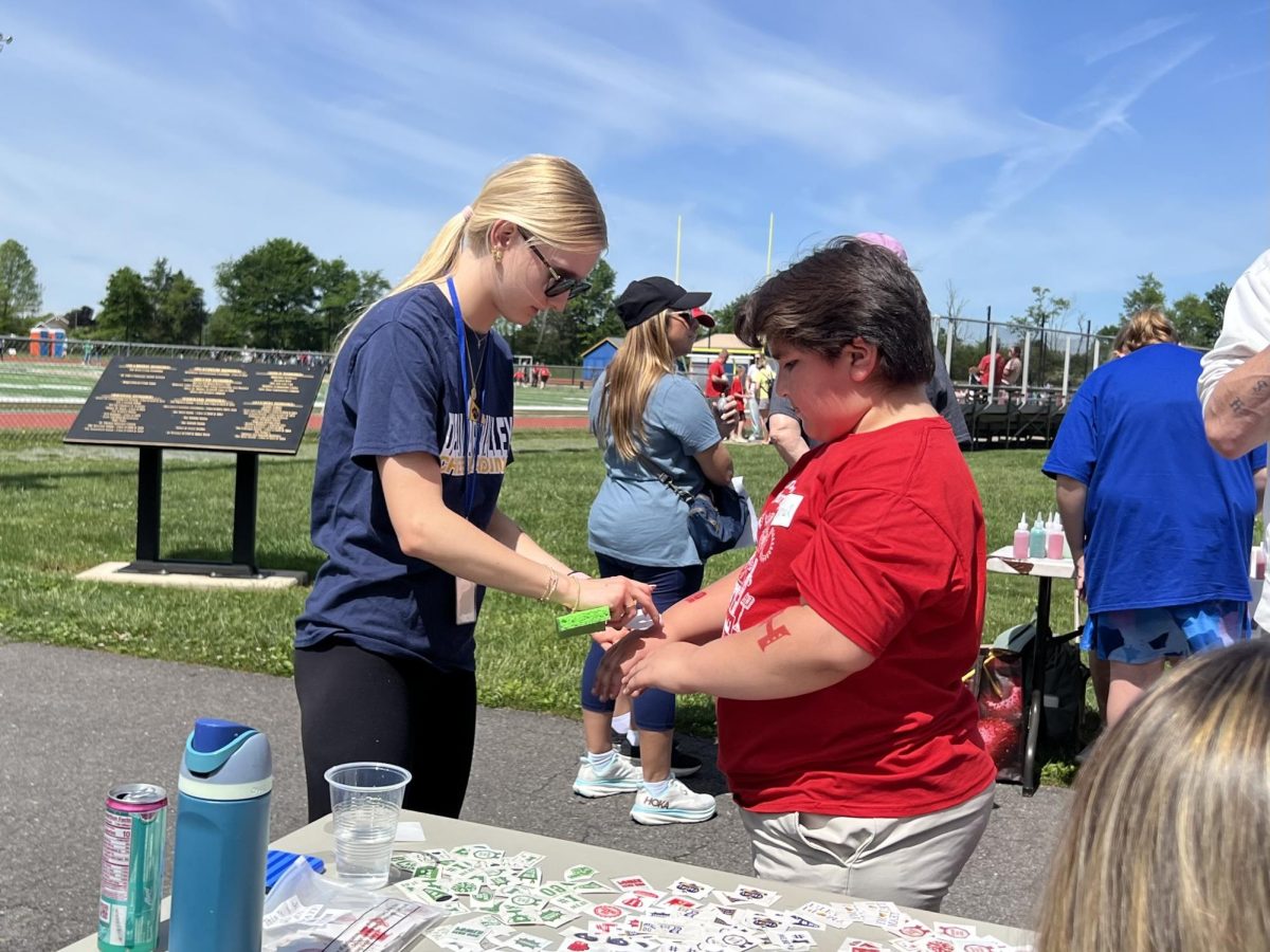 Jenna Sedlacek tattoos a Holland Township School student. Tournament of Champions had a variety of stations, including temporary tattoos, sprinting, javelin, sand art and long jump.