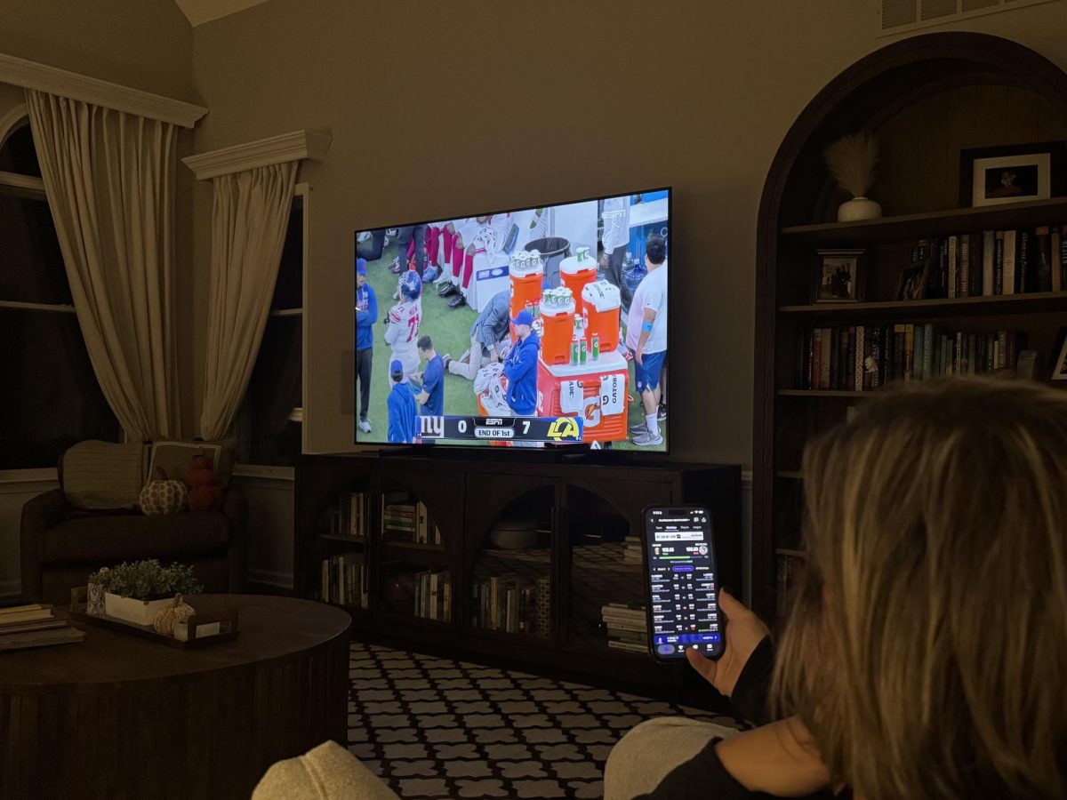 A fantasy football manager checks their lineup on their phone while watching the game unfold on TV.